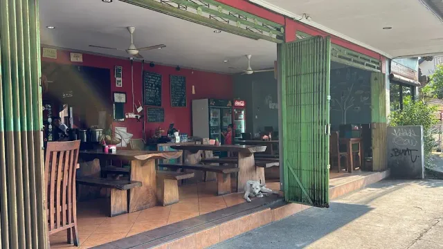 מסעדה פתוחה לרחוב עם קיר אדום, לוחות גיר, ספסלי עץ כבדים וכלב שוכב בכניסה