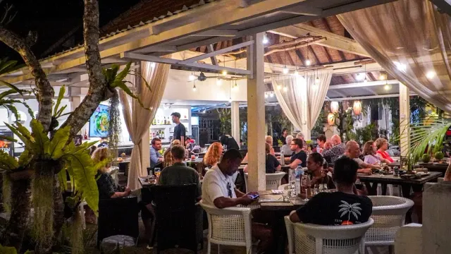 מסעדה פתוחה הומה בערב עם וילונות לבנים, גג רעפים וסועדים בשולחנות