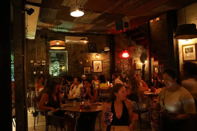 חלל כפרי אפלולי עם תקרת פח, קירות אבן מכוסים תמונות ממוסגרות ושולחנות מלאים
