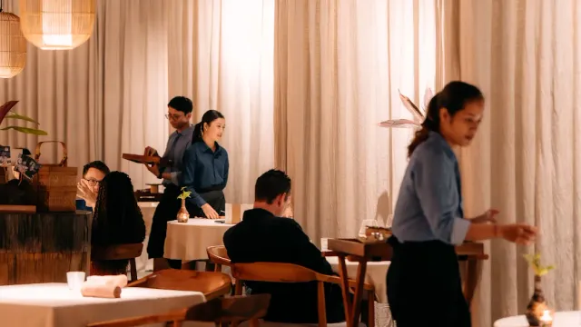 חלל מינימלי עם וילונות בז׳, אנשי שירות בחולצות כחולות ושולחנות קטנים באור עמום