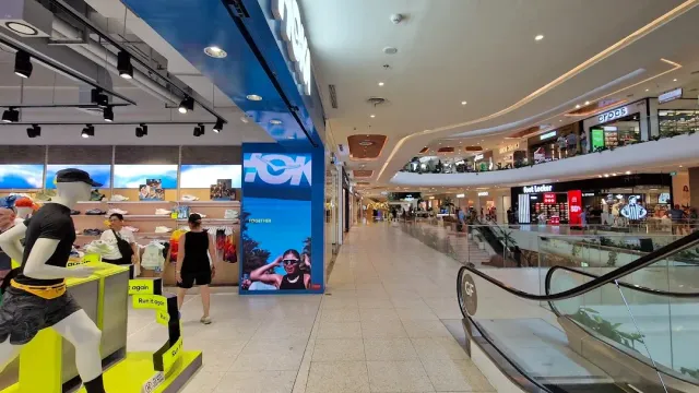 פנים קניון עם דרגנועים, חלונות ראווה, בובות תצוגה ומסך כחול גדול