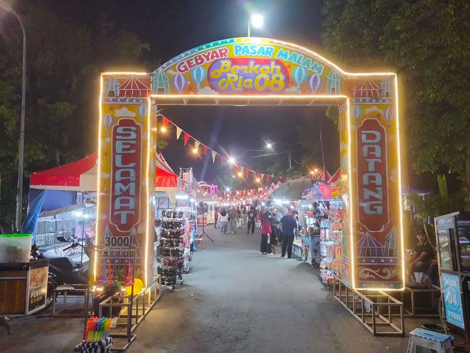דוכן אוכל רחוב בשוק לילה פסאר מלם בבאלי עם שיפודי סאטיי על גריל פחמים ועשן עולה, מוכר מקומי מכין מנות טריות בערב